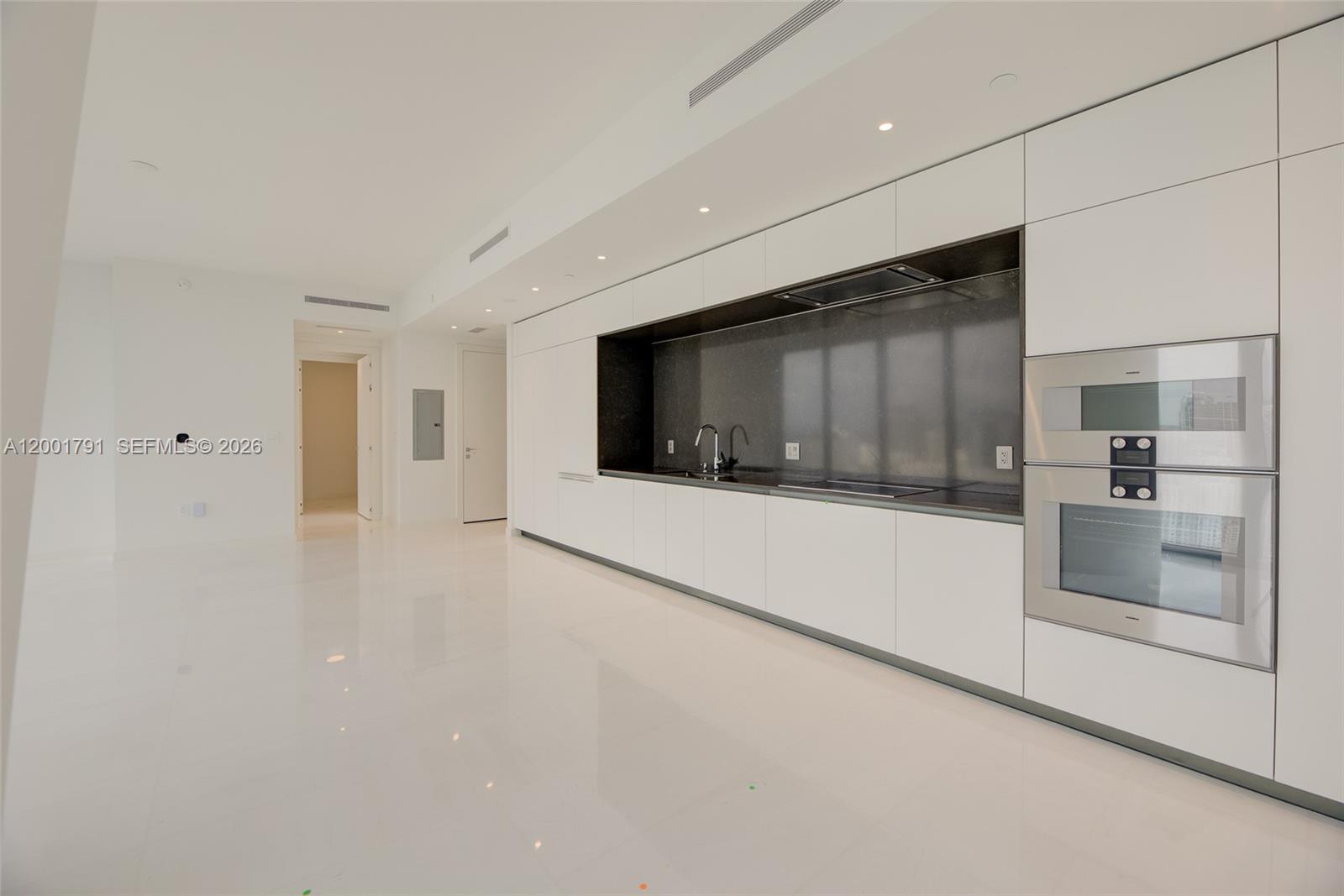 A modern kitchen features white cabinetry, a dark stone backsplash, and stainless steel built-in appliances — 300 Biscayne Boulevard Way # 4708W, Miami FL 33131, MIAMI, FL