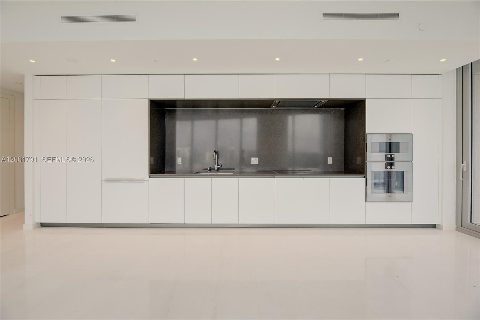 A modern kitchen features white flat-panel cabinetry, a dark stone backsplash, and stainless steel appliances — 300 Biscayne Boulevard Way # 4708W, Miami FL 33131, MIAMI, FL