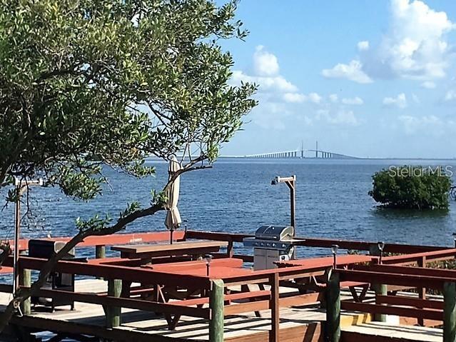 A wooden deck with a picnic table and grill overlooks the water and a distant bridge — 1515 PINELLAS BWY S UNIT 15, TIERRA VERDE, FL