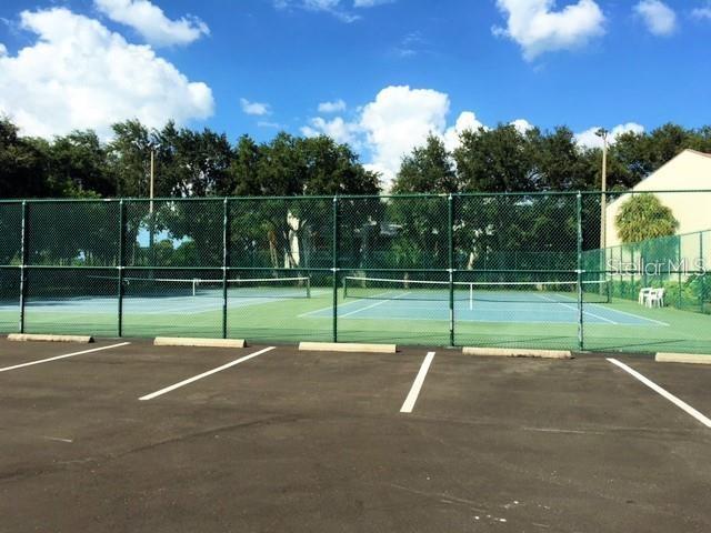 A fenced-in tennis court sits adjacent to a paved parking lot under a blue sky — 1515 PINELLAS BWY S UNIT 15, TIERRA VERDE, FL