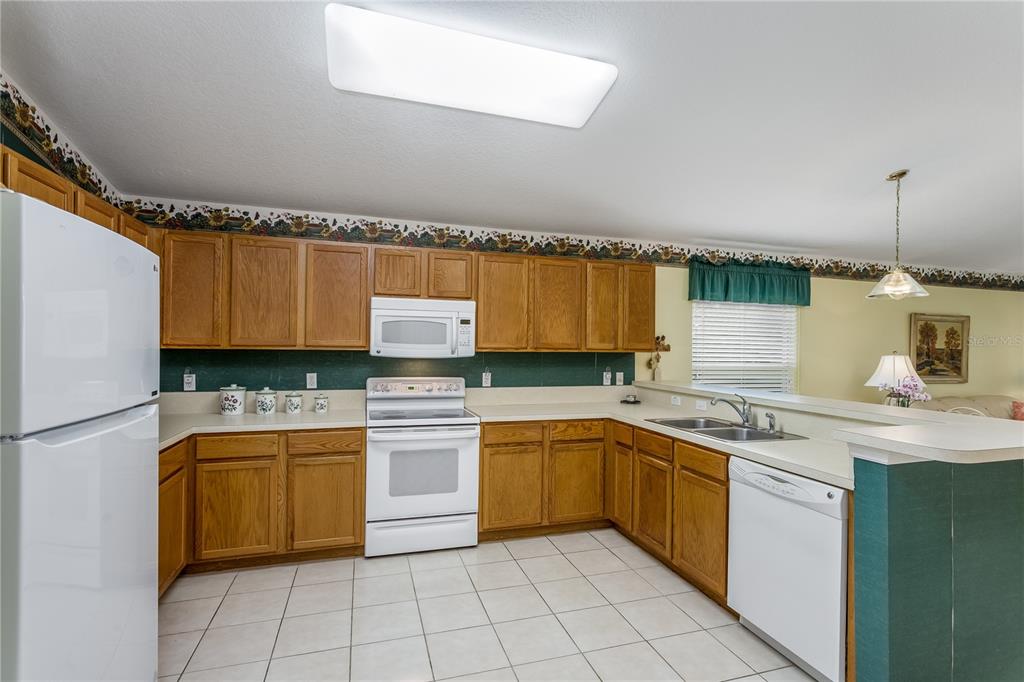 A kitchen with oak cabinets, white appliances, a tiled floor, and a green backsplash — 7845 GENOA LANE, LAND O LAKES, FL