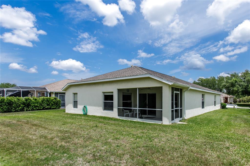 The rear exterior of a single-story house features a screened-in patio and a grassy yard — 7845 GENOA LANE, LAND O LAKES, FL