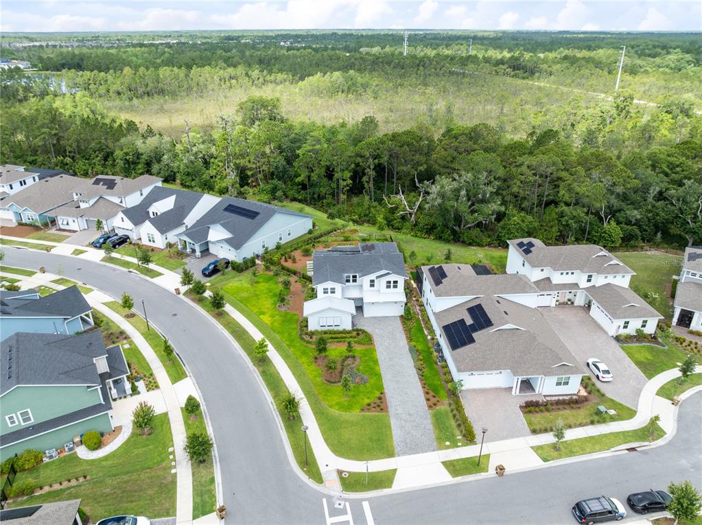 An aerial view shows several suburban houses with solar panels and driveways near a forest — 3122 VANGUARD COURT, ST CLOUD, FL