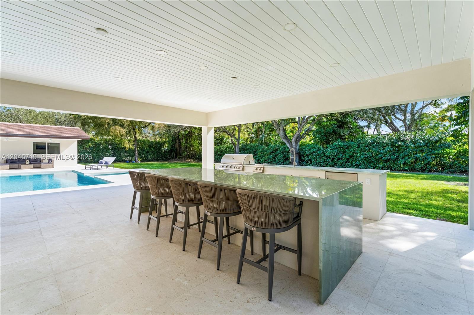 An outdoor kitchen features a stone island with bar seating under a covered patio — 6700 SW 117th St, Pinecrest FL 33156, PINECREST, FL