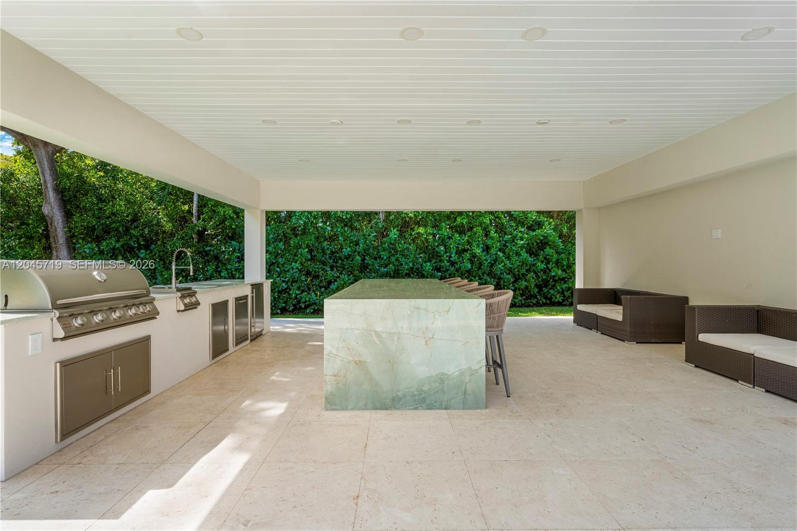 An outdoor kitchen features a stone island, stainless steel grill, and lounge seating under a roof — 6700 SW 117th St, Pinecrest FL 33156, PINECREST, FL