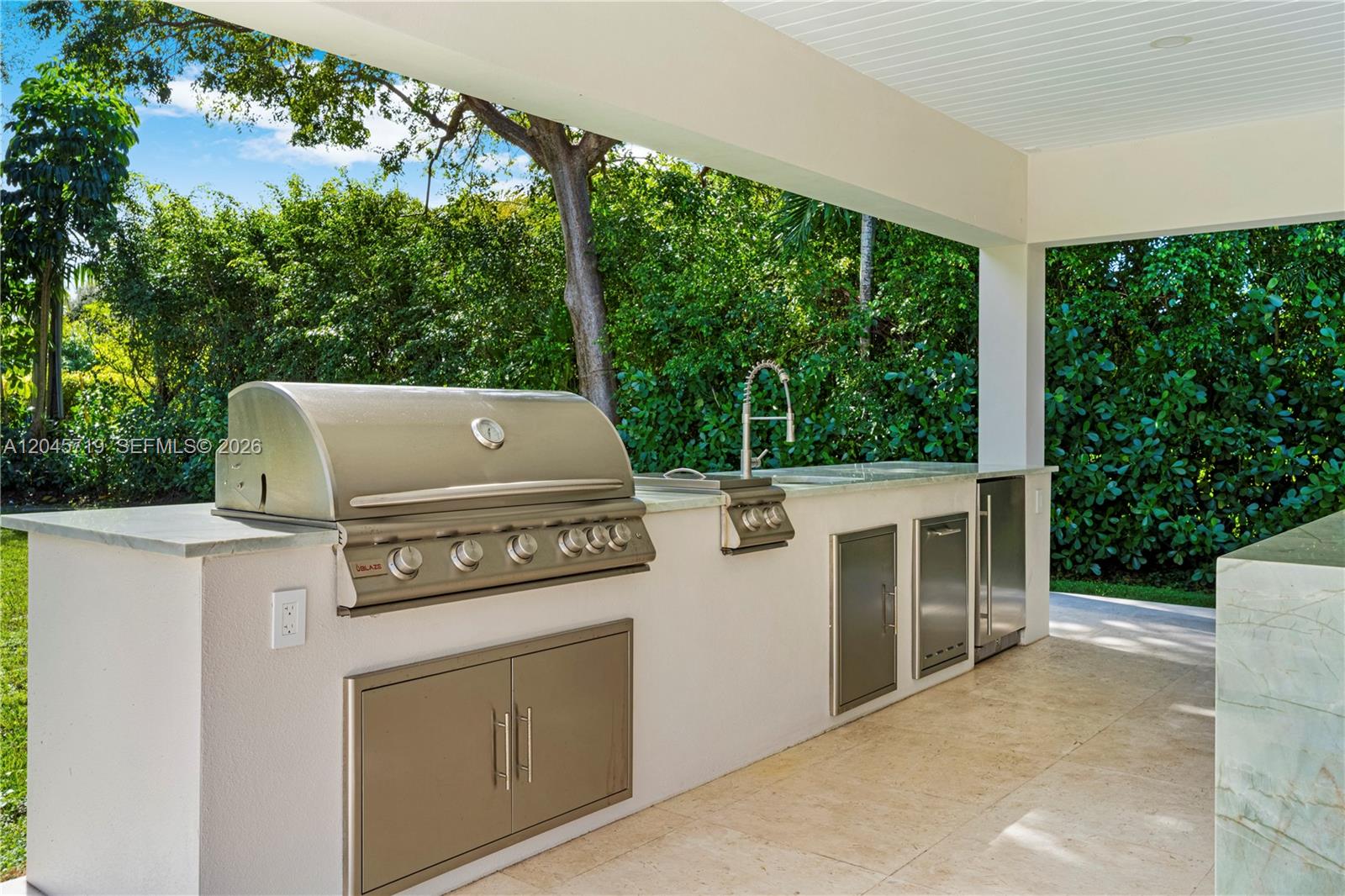 An outdoor kitchen features a stainless steel grill, sink, and cabinetry under a covered patio — 6700 SW 117th St, Pinecrest FL 33156, PINECREST, FL