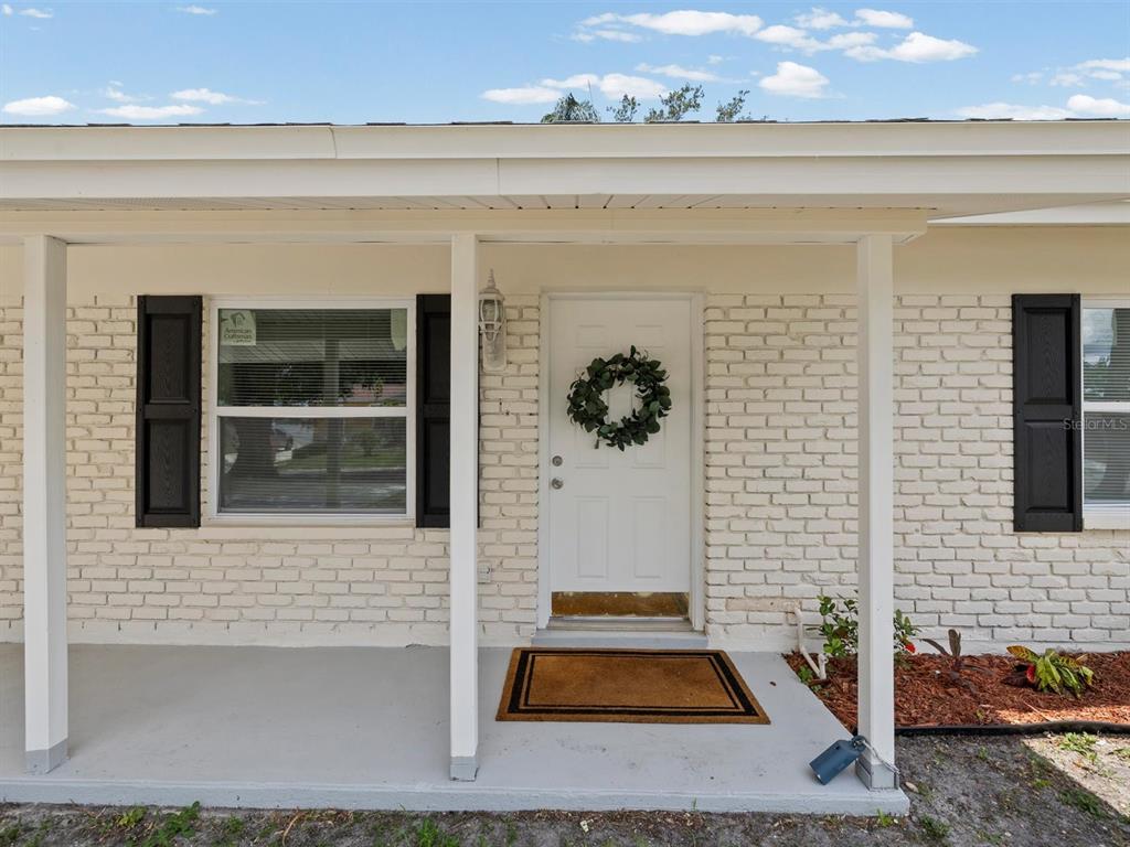 A white brick house exterior features a covered front porch, a white door, and shutters — 4928 SHETLAND AVENUE, TAMPA, FL