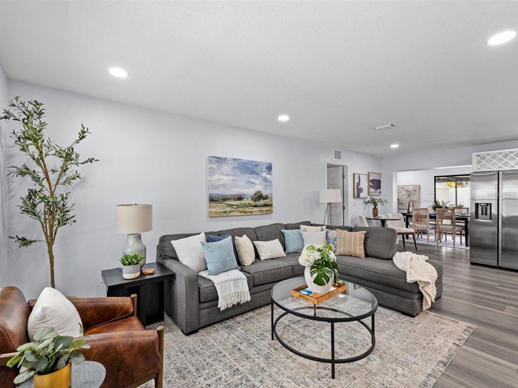 A living room features a gray sectional sofa, a glass coffee table, and wood-look flooring — 4928 SHETLAND AVENUE, TAMPA, FL