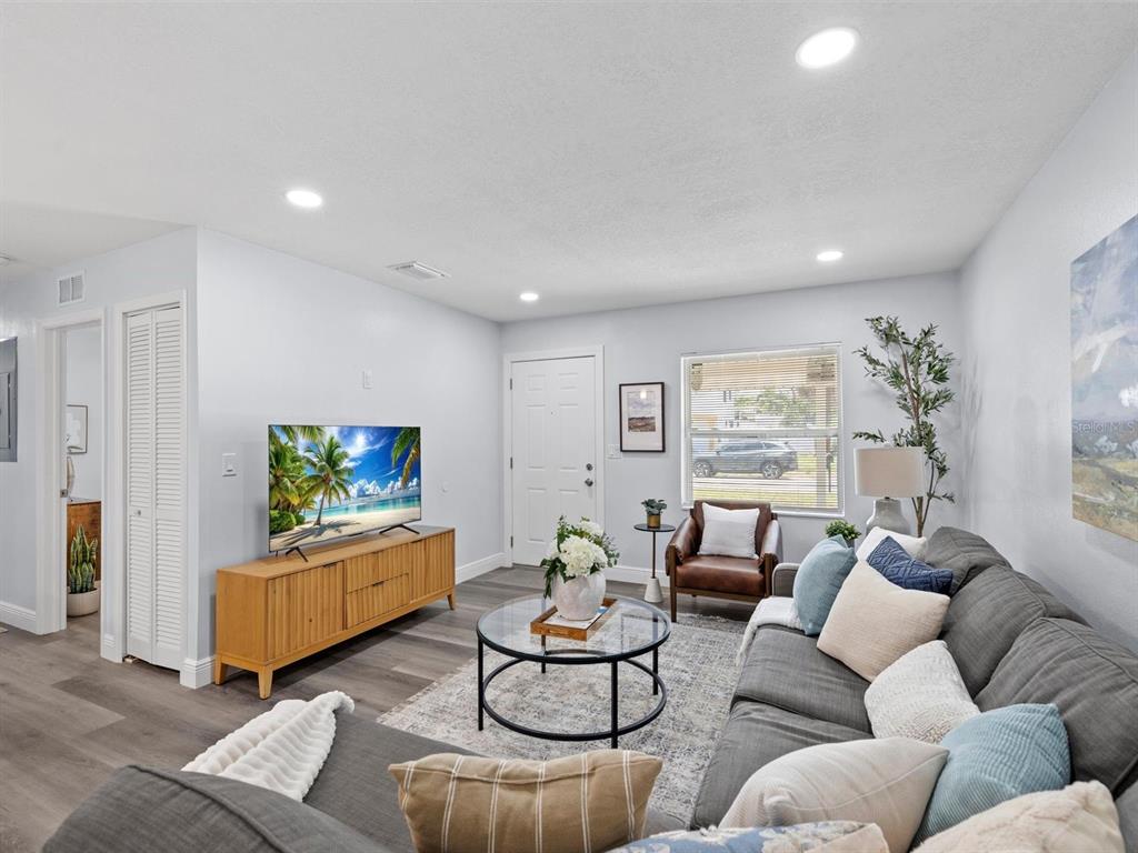A living room features gray flooring, a sectional sofa, a glass coffee table, and a television — 4928 SHETLAND AVENUE, TAMPA, FL