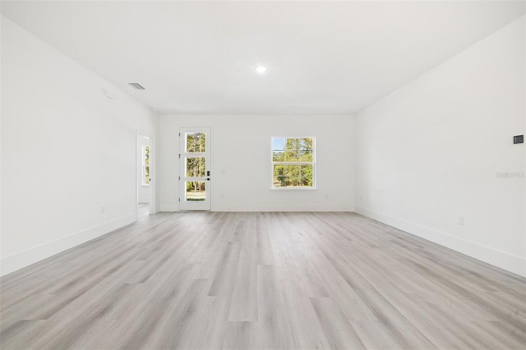 A bright, empty room features white walls, light gray wood-look flooring, and a glass-paneled door — 9571 N OLD MILL WAY, CITRUS SPRINGS, FL