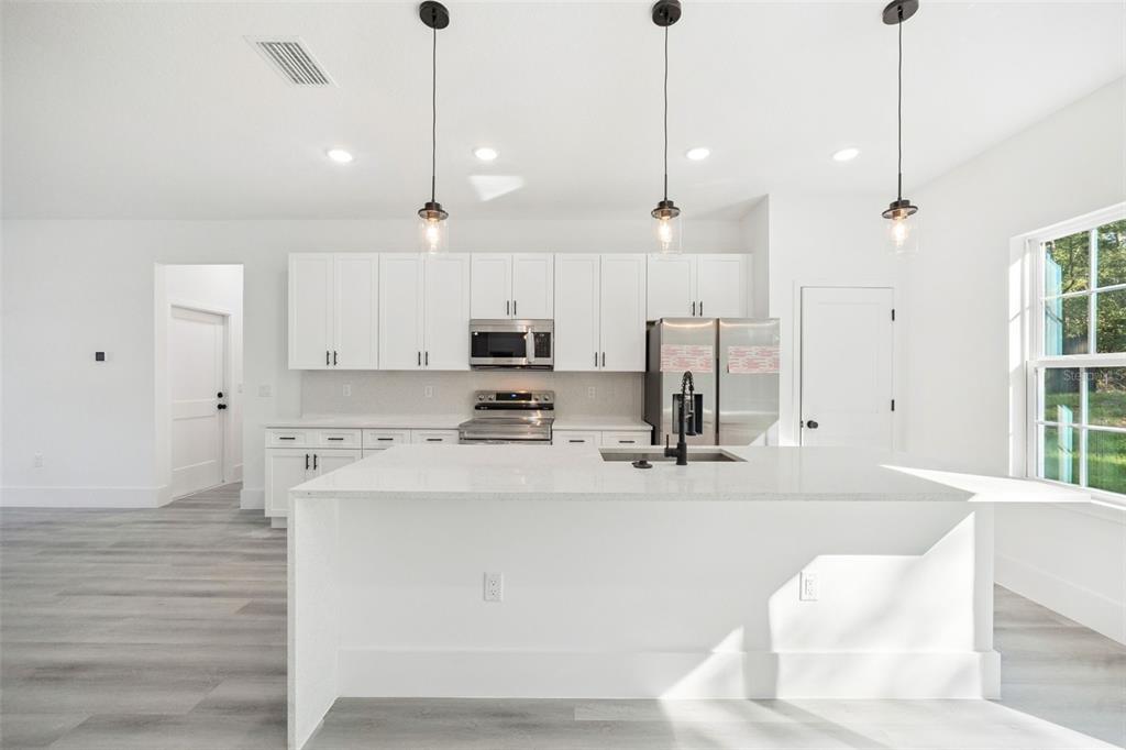 A modern white kitchen features a large island, stainless steel appliances, and gray wood flooring — 9571 N OLD MILL WAY, CITRUS SPRINGS, FL