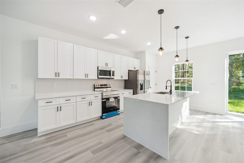 A modern kitchen features white cabinetry, stainless steel appliances, a quartz island, and light flooring — 9571 N OLD MILL WAY, CITRUS SPRINGS, FL