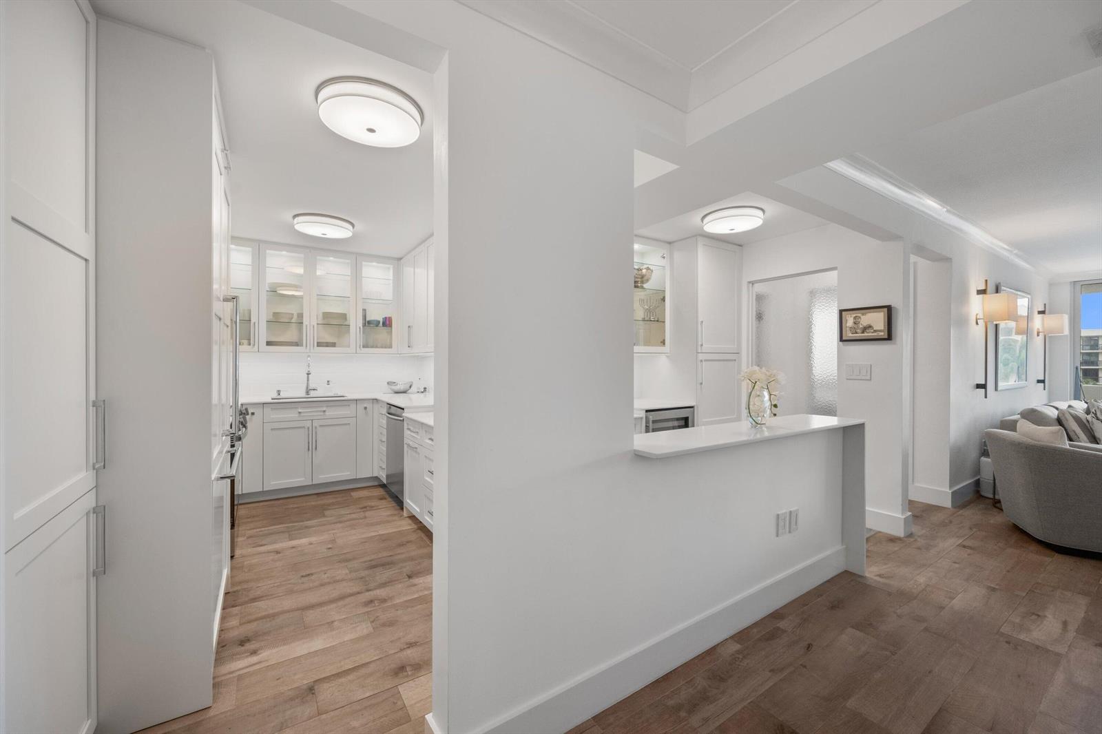 A white kitchen with wood floors opens to a living area with a breakfast bar — 2773 S Ocean Boulevard # 410, Palm Beach FL 33480, PALM BEACH, FL