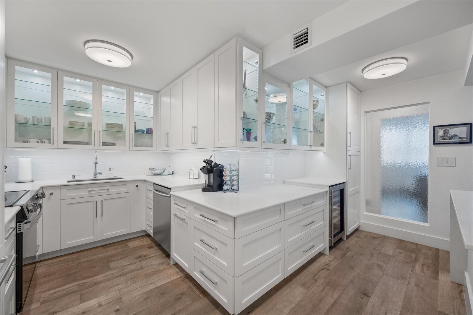 A white kitchen features glass-front cabinets, stainless steel appliances, and light wood-look flooring — 2773 S Ocean Boulevard # 410, Palm Beach FL 33480, PALM BEACH, FL