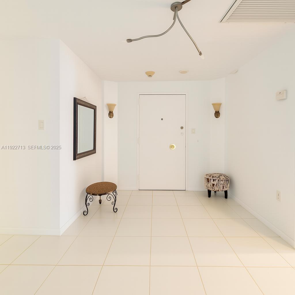 This entryway features white tiled floors, a central door, two small stools, and wall sconces — 5255 Collins Ave # 5D, Miami Beach FL 33140, MIAMI BEACH, FL