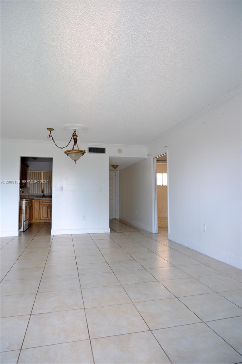 An empty room with beige tile flooring, white walls, and a hanging light fixture — 650 NE 149th St # 505F, Miami FL 33161, MIAMI, FL