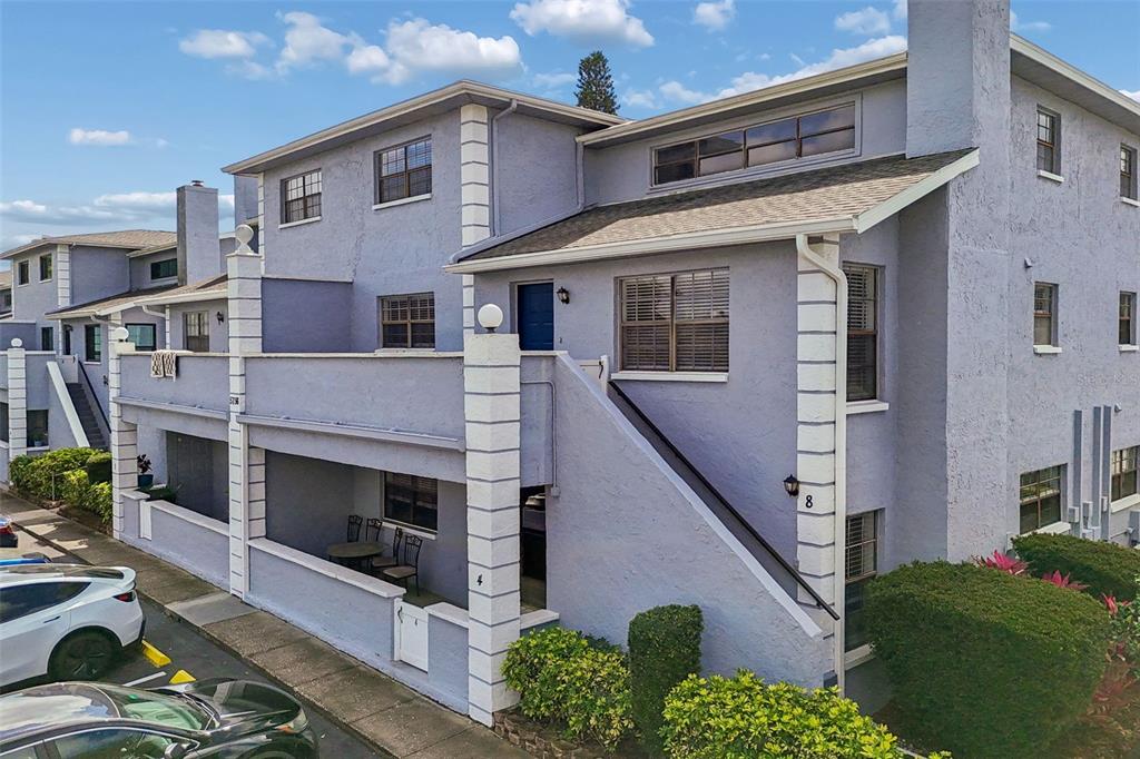 The exterior of a multi-story, light purple stucco apartment building features a covered patio — 5756 CALAIS BOULEVARD N UNIT 8, ST PETERSBURG, FL