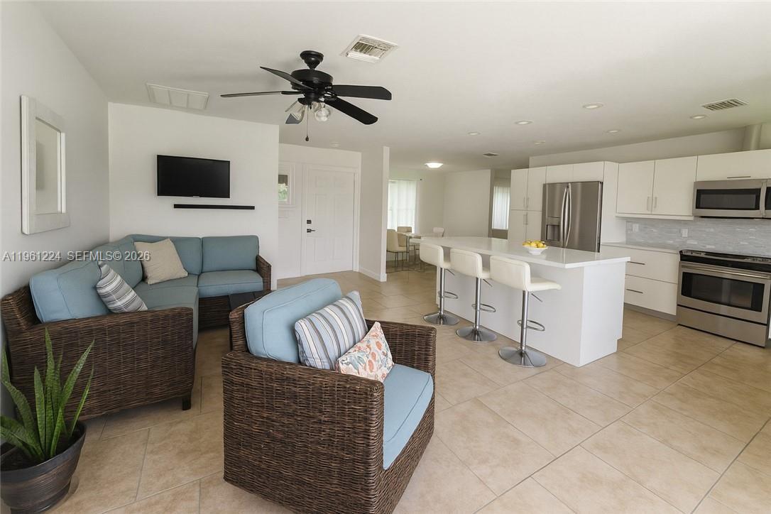 An open-concept living room and kitchen feature light tile floors and white cabinetry — 5010 SW 31st AVE, Naples FL 34116, NAPLES, FL