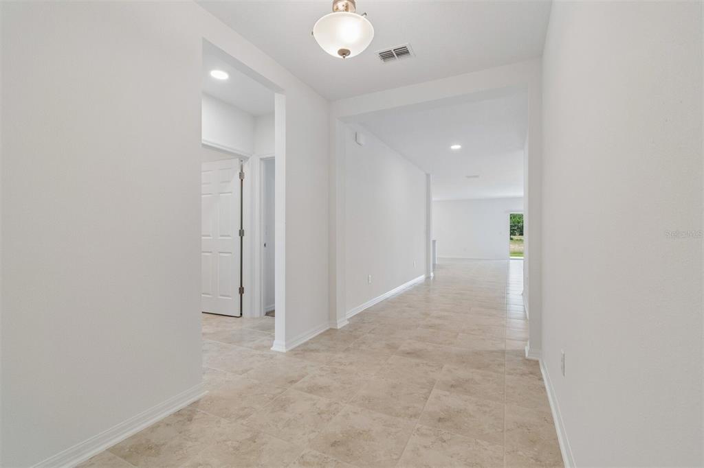 A bright hallway with light tile flooring leads toward an open living area — 8461 FOX DEN COVE, LAKELAND, FL