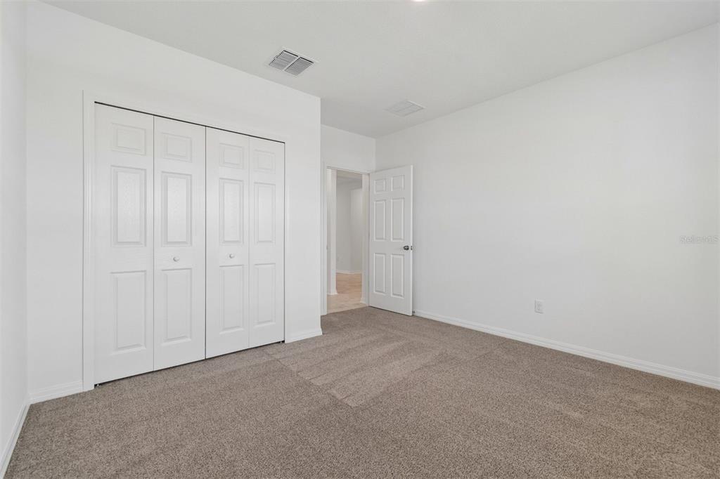 A bedroom with white walls, beige carpet, a white closet, and an open doorway — 8461 FOX DEN COVE, LAKELAND, FL