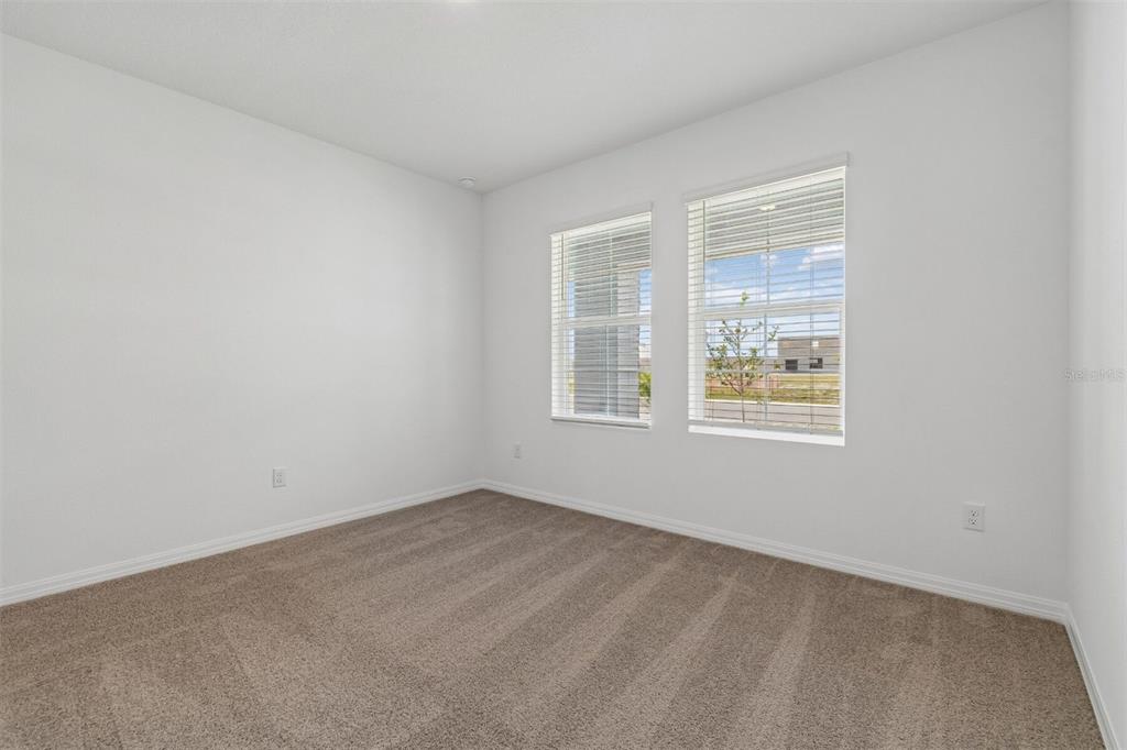 An empty bedroom features white walls, tan carpeting, and two windows with white blinds — 8461 FOX DEN COVE, LAKELAND, FL