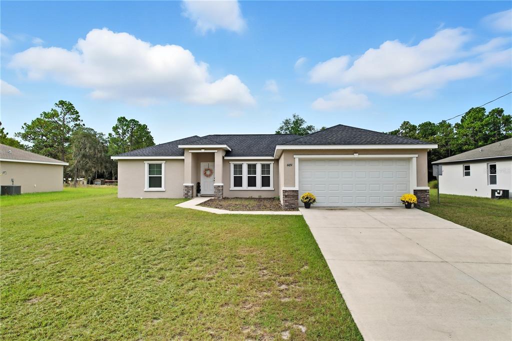 A single-story house with a beige stucco exterior, a two-car garage, and a concrete driveway — 6651 SW 151ST LOOP, OCALA, FL