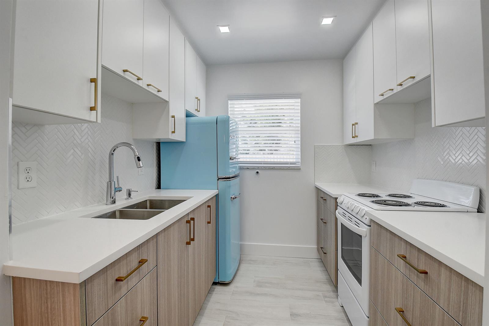 A galley kitchen features white upper cabinets, wood-tone lower cabinets, and a light blue refrigerator — 502 N H Street # 4, FL 33460, FL
