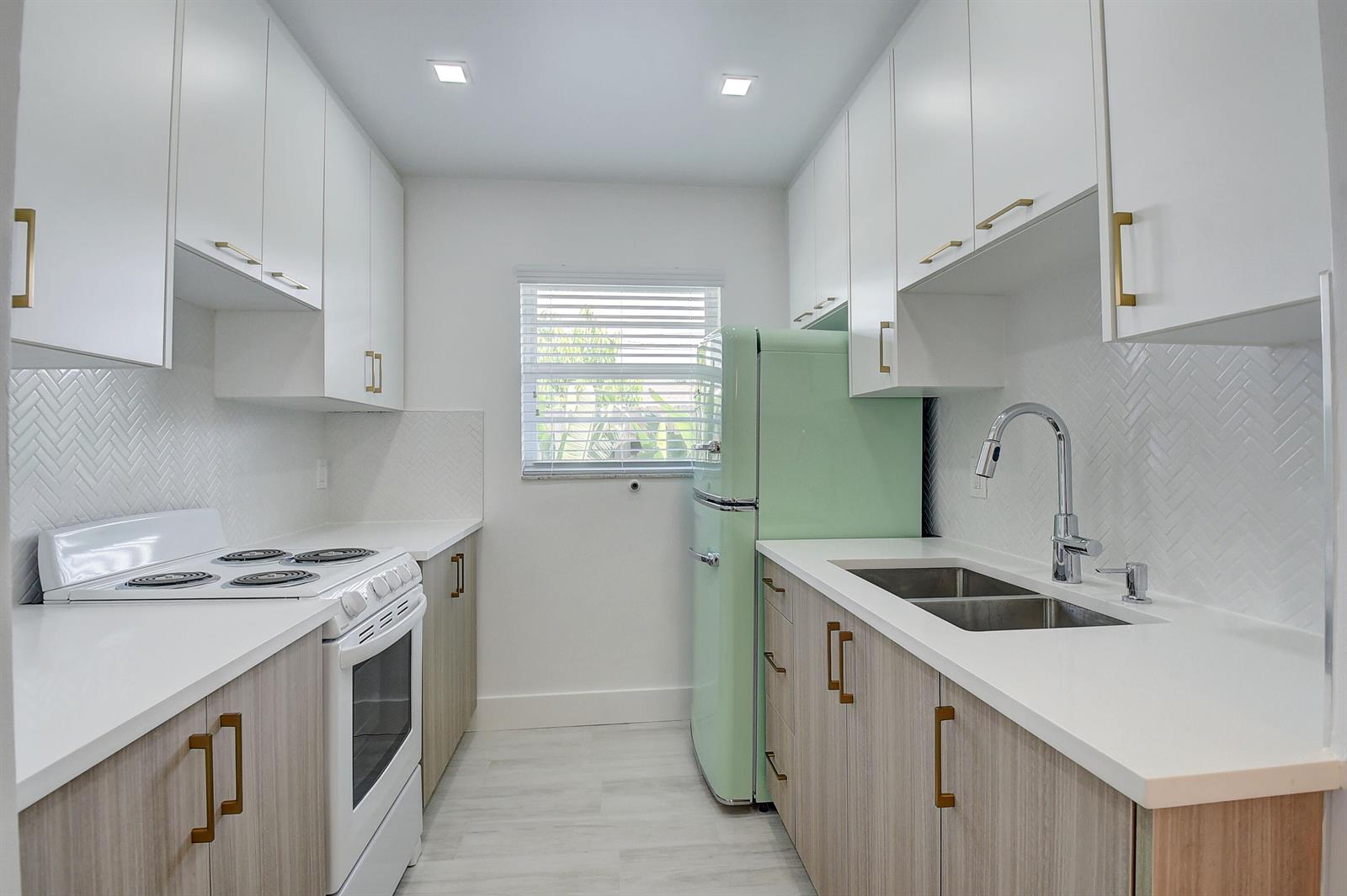 A galley kitchen features white upper cabinets, wood-tone lower cabinets, white countertops, and a green refrigerator — 502 N H Street # 4, FL 33460, FL