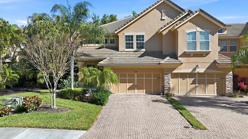 A two-story tan stucco townhouse with a paver driveway and two garage doors — 5427 NAPA DRIVE, SARASOTA, FL