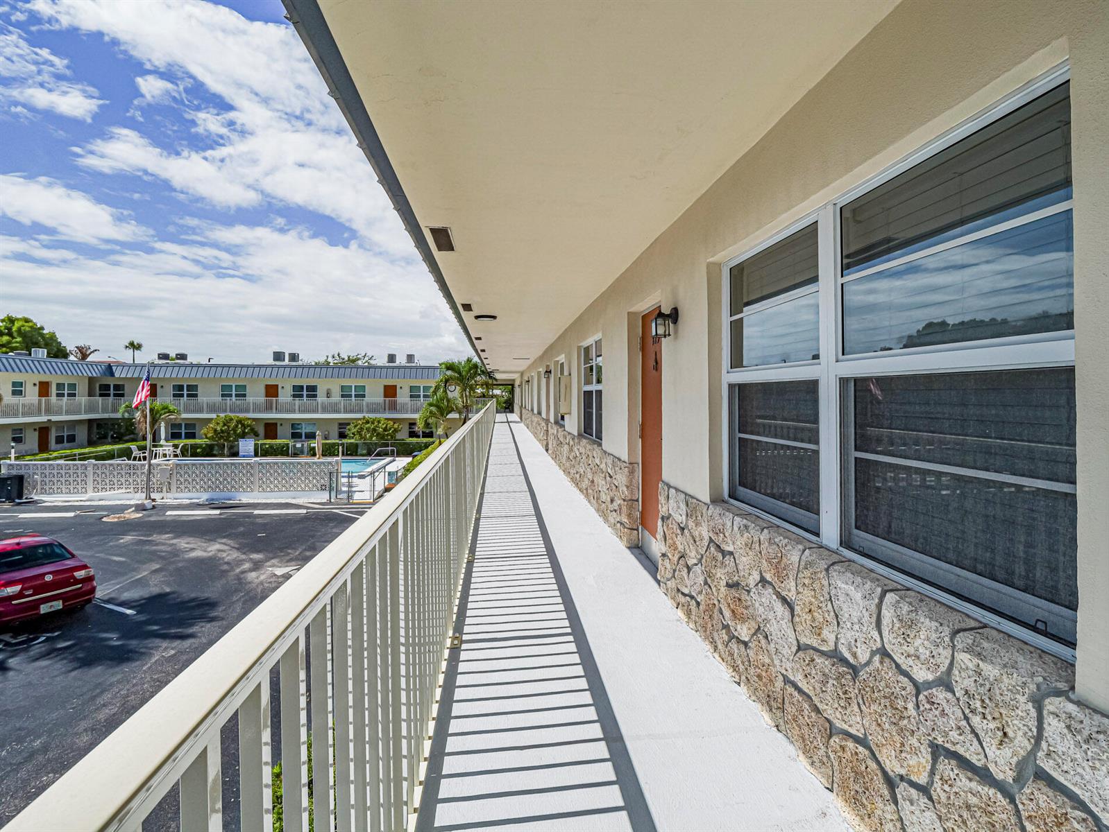 An exterior walkway with stone accents overlooks a parking lot and a swimming pool — 923 22nd Place # 219, Vero Beach FL 32960, VERO BEACH, FL