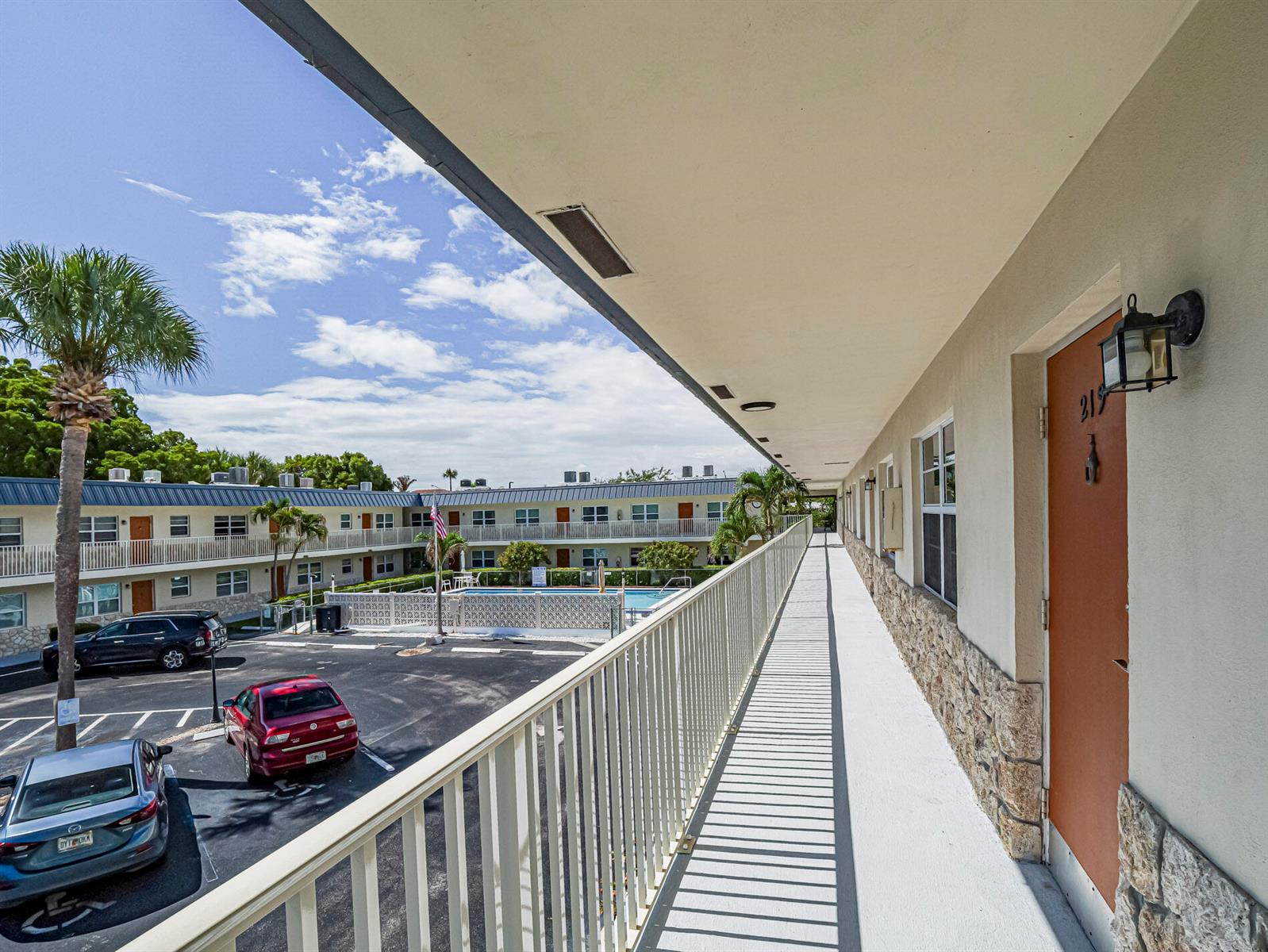 An exterior walkway overlooks a parking lot and swimming pool at a multi-story apartment complex — 923 22nd Place # 219, Vero Beach FL 32960, VERO BEACH, FL