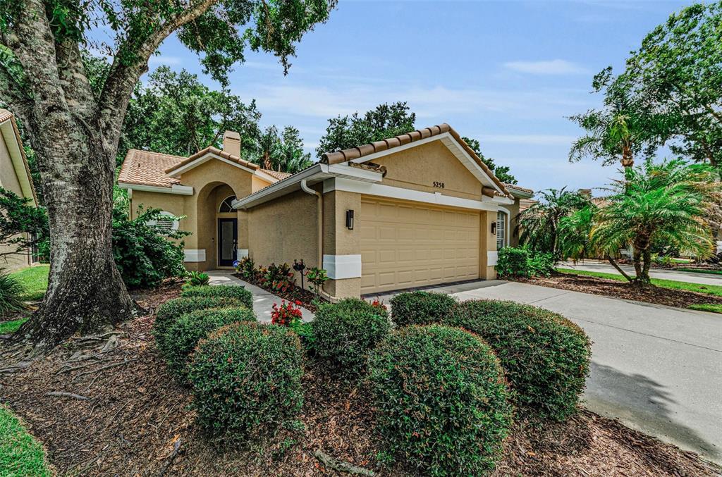 A tan single-story house with a two-car garage and landscaped front yard — 5250 PINEHURST COURT, OLDSMAR, FL