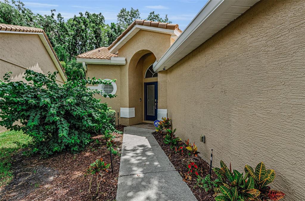 A concrete walkway leads to the arched entryway of a tan stucco house — 5250 PINEHURST COURT, OLDSMAR, FL