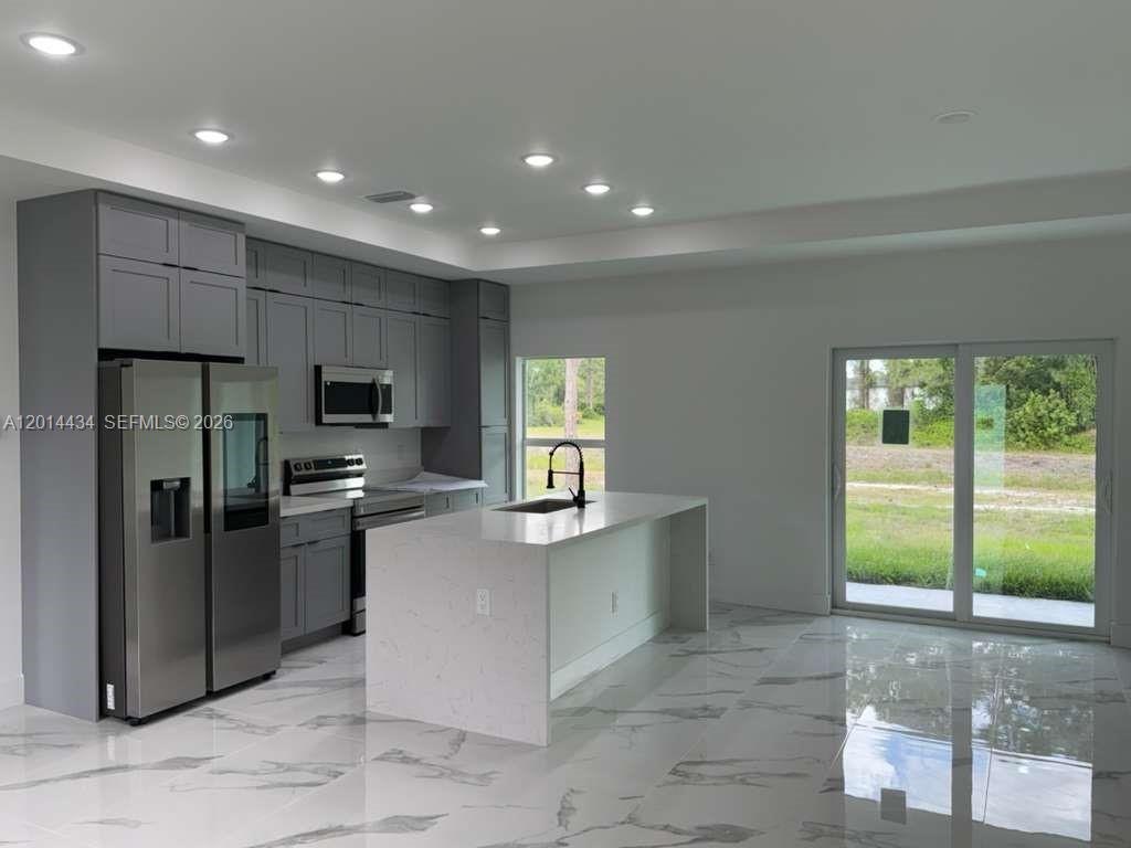 A modern kitchen features gray cabinets, a white quartz island, and large floor tiles — 765 PUCCINI AVE S, Lehigh Acres FL 33974, LEHIGH ACRES, FL