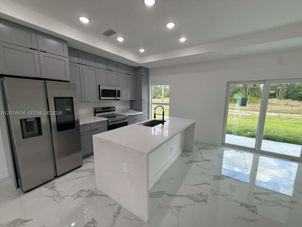 A modern kitchen features gray cabinets, a white quartz island, and large sliding glass doors — 765 PUCCINI AVE S, Lehigh Acres FL 33974, LEHIGH ACRES, FL