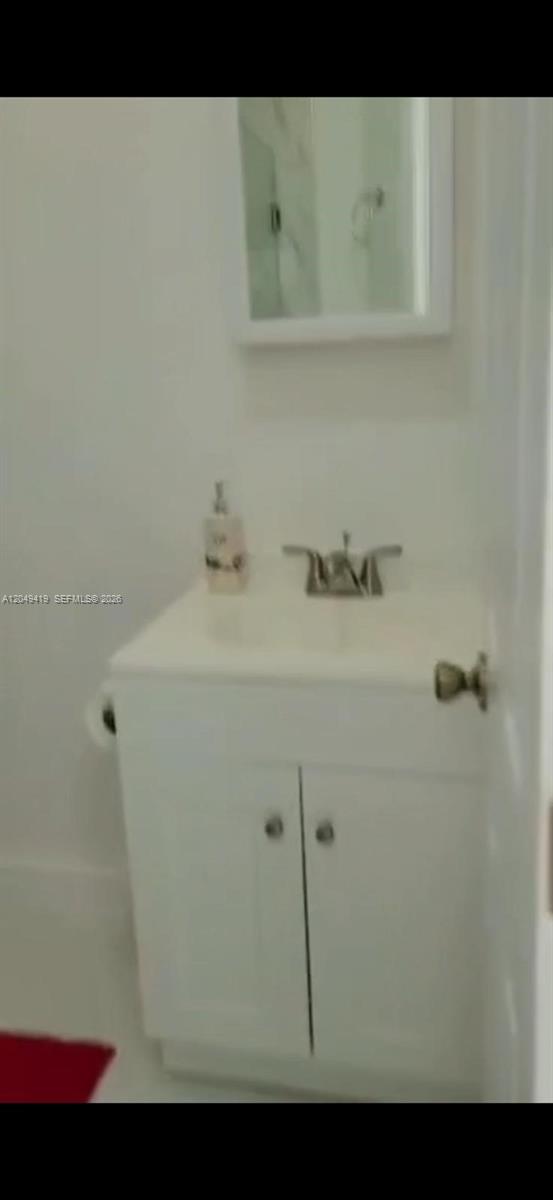 A small bathroom features a white vanity cabinet with a sink and a wall mirror — MIAMI, FL