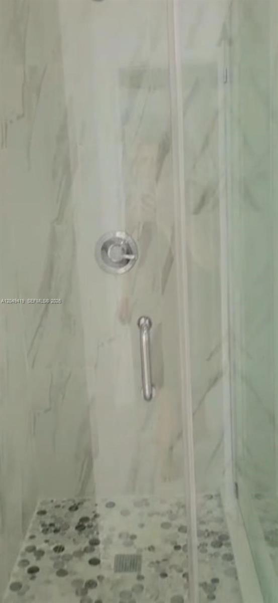 A walk-in shower features marble-look wall tiles, a pebble-stone floor, and chrome fixtures — MIAMI, FL