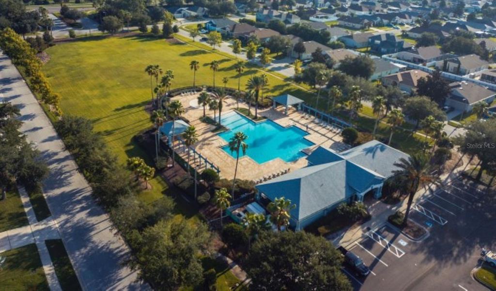 An aerial view of a community swimming pool, clubhouse, and parking lot surrounded by houses — 7627 STONEY HILL DRIVE, WESLEY CHAPEL, FL