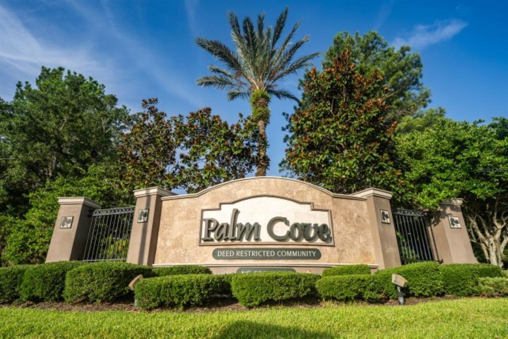 A stone entrance sign for Palm Cove deed restricted community stands before trees and landscaping — 7627 STONEY HILL DRIVE, WESLEY CHAPEL, FL