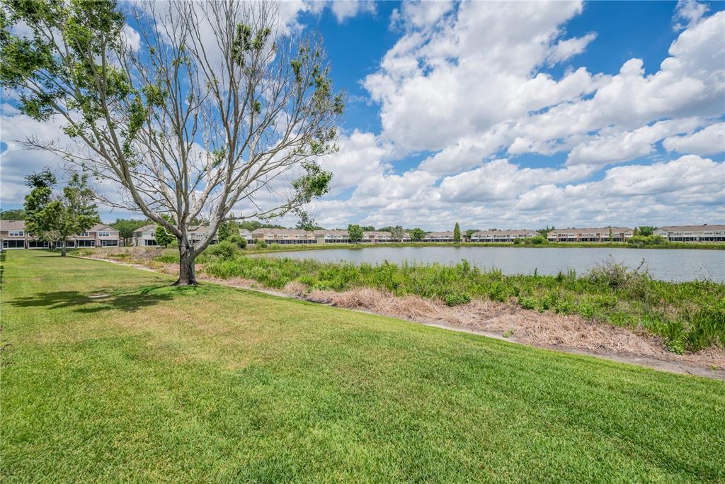 A grassy lawn leads to a pond with a line of townhomes in the background — 4939 POND RIDGE DRIVE, RIVERVIEW, FL