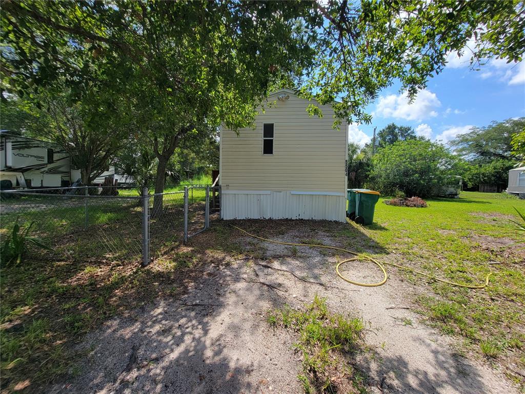 The exterior of a light-colored mobile home features a single window and a gravel yard — 5504 WILSON DRIVE, PUNTA GORDA, FL