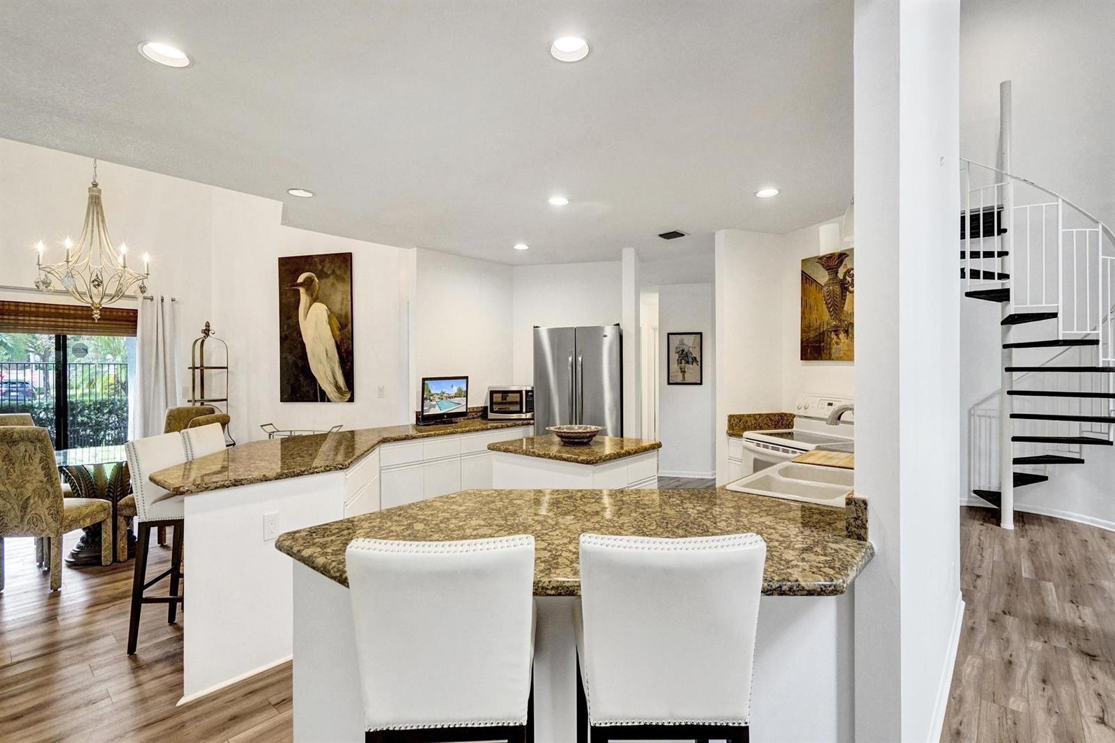A kitchen features granite countertops, white cabinetry, stainless steel appliances, and a spiral staircase nearby — 23417 Water Circle, Boca Raton FL 33486, BOCA RATON, FL