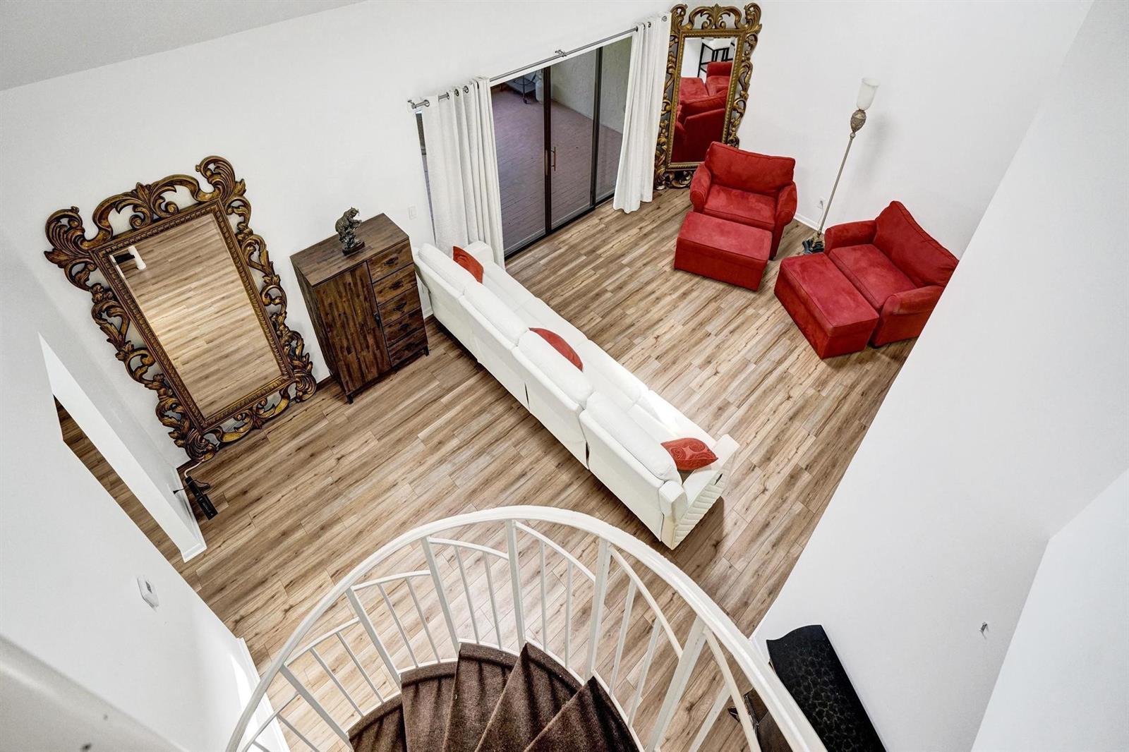 A high-angle view of a living room featuring a spiral staircase, white sofa, and two red armchairs — 23417 Water Circle, Boca Raton FL 33486, BOCA RATON, FL