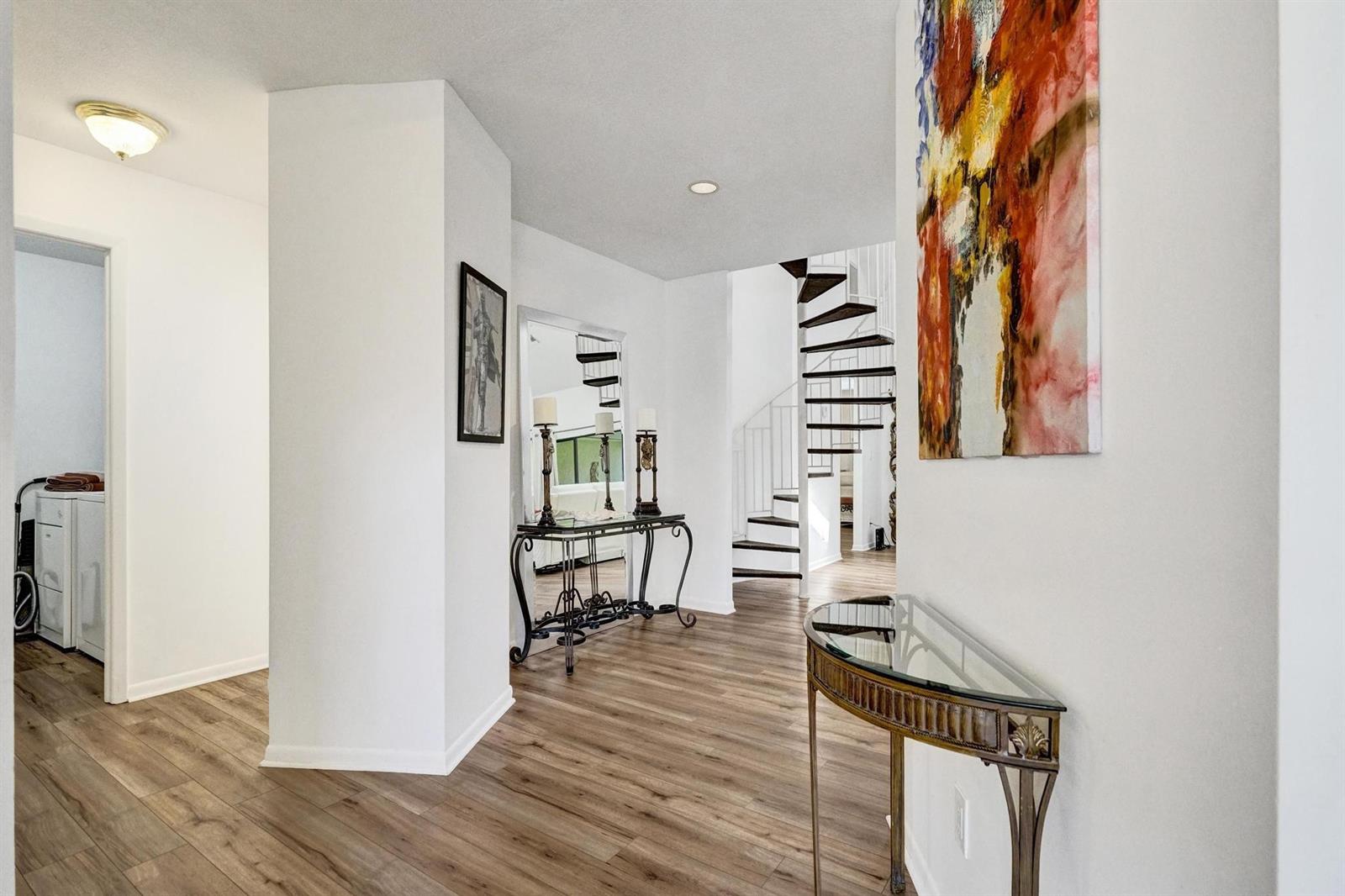 A bright entryway features wood-look flooring, a glass-topped console table, and a spiral staircase — 23417 Water Circle, Boca Raton FL 33486, BOCA RATON, FL