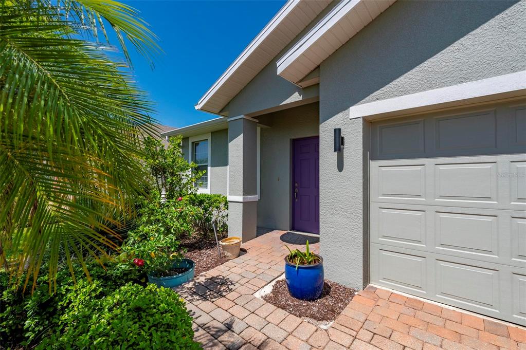 A house exterior features a purple front door, a gray garage door, and a brick walkway — 24604 RIO VILLA LAKES CIRCLE, PUNTA GORDA, FL