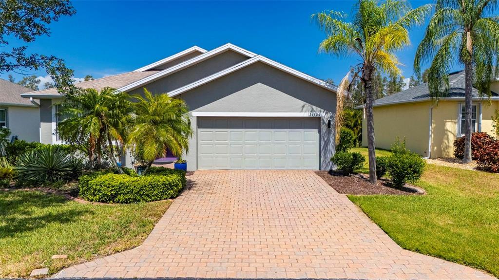 A single-story house with a gray garage, a paved driveway, and palm trees in front — 24604 RIO VILLA LAKES CIRCLE, PUNTA GORDA, FL