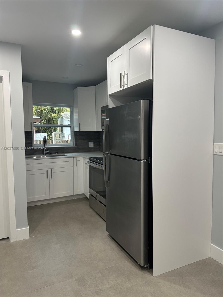 A kitchen features white cabinets, stainless steel appliances, gray tile flooring, and a window — 1628 NW 15th St # A, Miami FL 33125, MIAMI, FL