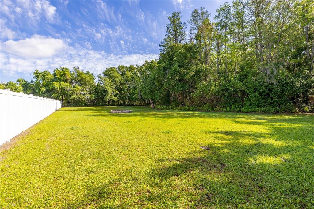 A grassy backyard features a white vinyl fence and a stone fire pit — 2507 WINNERS CIRCLE, KISSIMMEE, FL