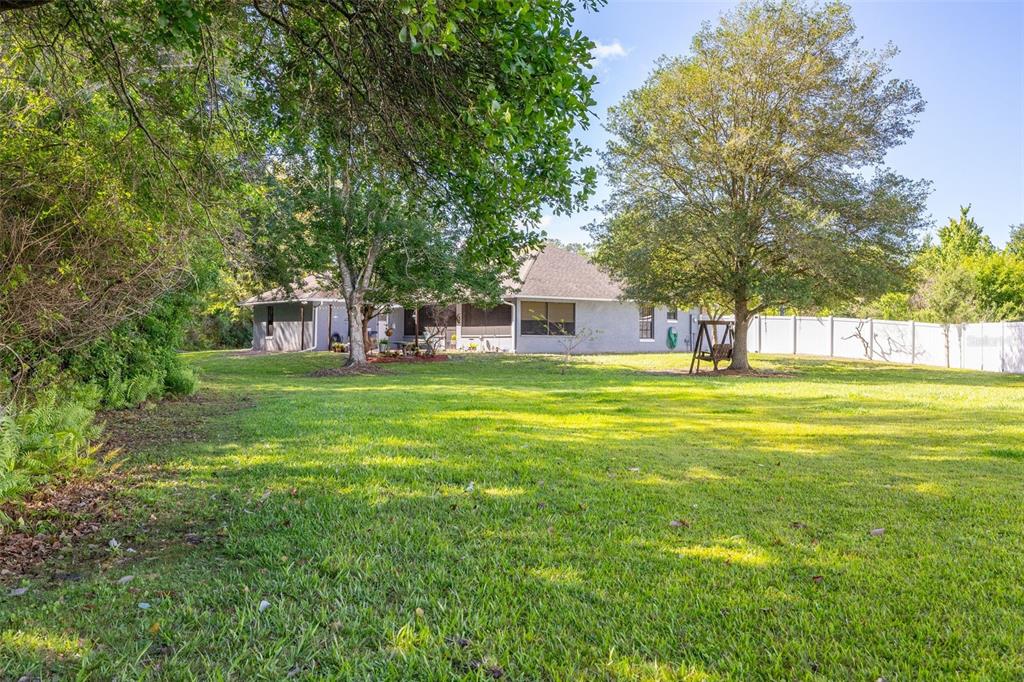 A backyard view of a single-story house with a large lawn and mature trees — 2507 WINNERS CIRCLE, KISSIMMEE, FL