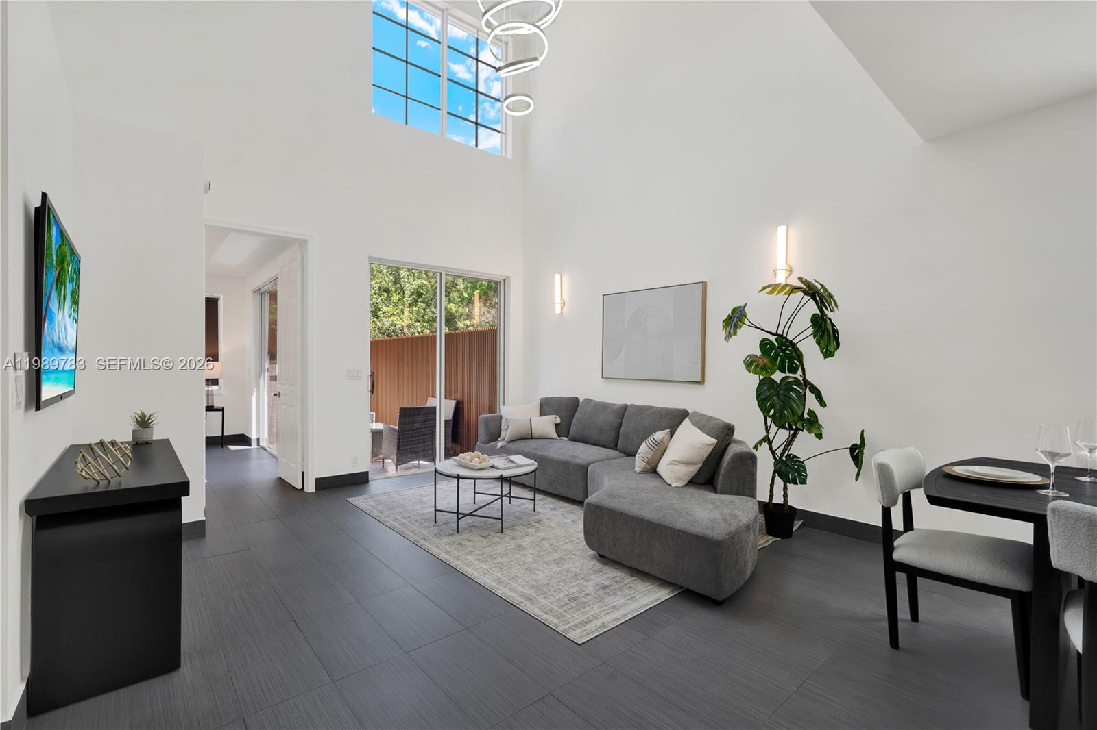 A modern living room features high ceilings, gray tile floors, a sectional sofa, and windows — 1251 Hayes St, Hollywood FL 33019, HOLLYWOOD, FL